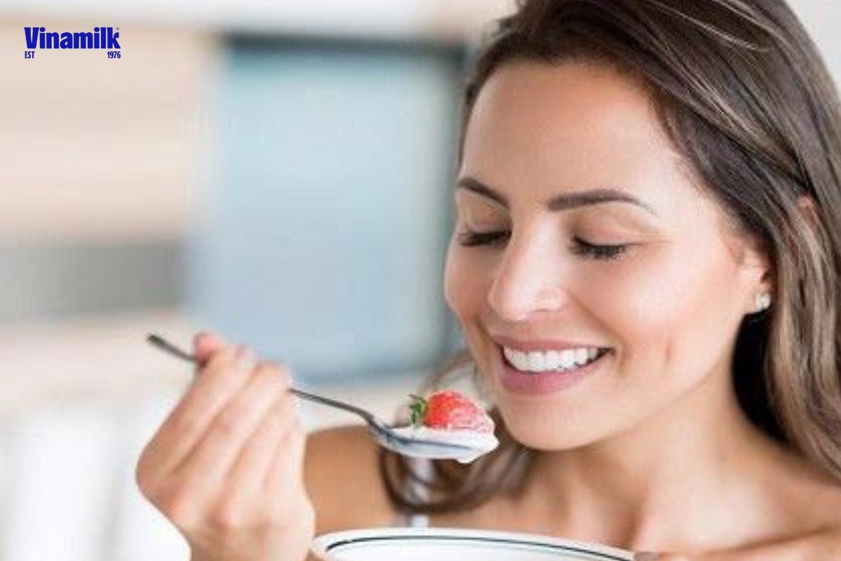 Người phụ nữ ăn sữa chua và tươi cười, tượng trưng cho làn da đẹp khỏe mạnh
