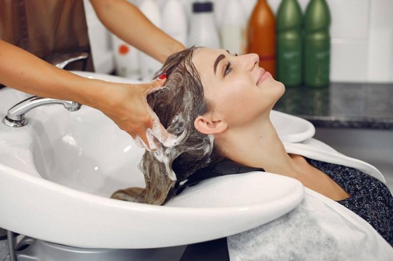 Hình ảnh cận cảnh một kỹ thuật viên đang thực hiện massage đầu cho khách hàng trong một tiệm gội đầu dưỡng sinh, tập trung vào các động tác chuyên nghiệp và không gian thư giãn.